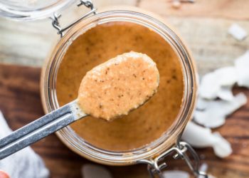 Overhead shot of a jar of homemade coconut butter with a hand spooning out a spoonful.