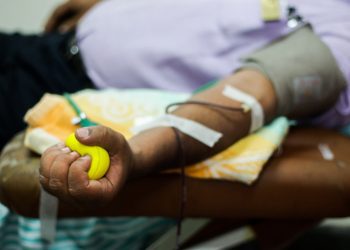 Midsection of a man in violet shirt giving a blood donation, arm is outstretched, hand is squeezing yellow ball
