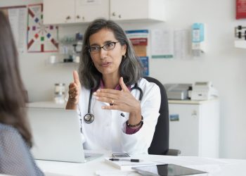 A female doctor discussing care with a woman in a health care office with charts on the wall