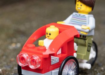 This picture shows a LEGO on a bike with a stroller attached.