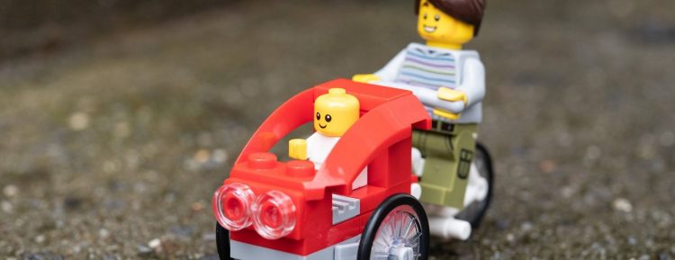 This picture shows a LEGO on a bike with a stroller attached.
