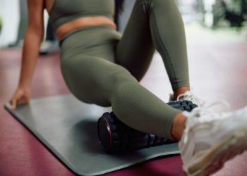 Woman uses foam roller on leg while exercising in a gym.