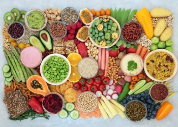 A brightly colored selection of plant-based vegan foods, including vegetables, fruit, grains, nuts, seeds, and vegan dips.
