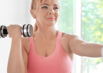 Middle age woman in pink workout top holding dumbbells