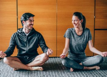 Couple sitting in lotus position, looking at each other and laughing.