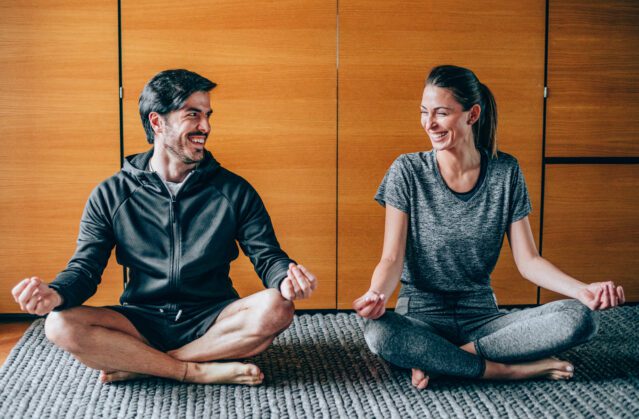 Couple sitting in lotus position, looking at each other and laughing.