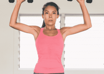 Young woman in pink shirt performing a standing dumbbell Arnold press