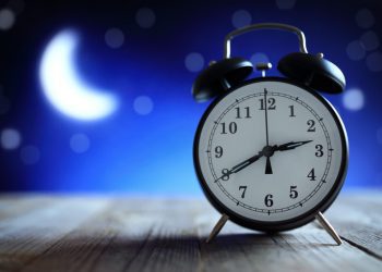 Alarm clock on wood table shows 2:40 am; on dark blue background is crescent moon and fuzzy stars, concept is insomnia