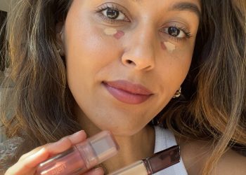A woman holding a cleaner and liquid blush with a white tank top on