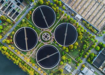 Aerial view of four tanks at a wastewater treatment plant with green trees and large-scale equipment dotted around the landscape