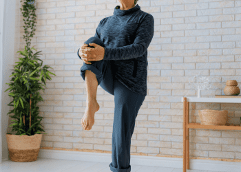 Senior woman performing hip strengthening exercises in living room with dumbbells and laptop