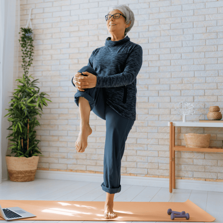 Senior woman performing hip strengthening exercises in living room with dumbbells and laptop