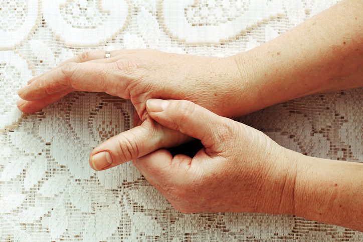 A woman's hands and forearms on a background of lace; painful arthritis in the thumb joint