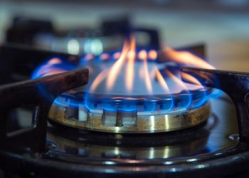 A gas stove burner with blue and yellowish flames; another burner in the background is blurred