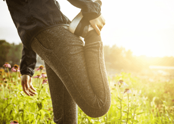 Side view of woman performing leg stretches in leggings, tennis shoes and track jacket
