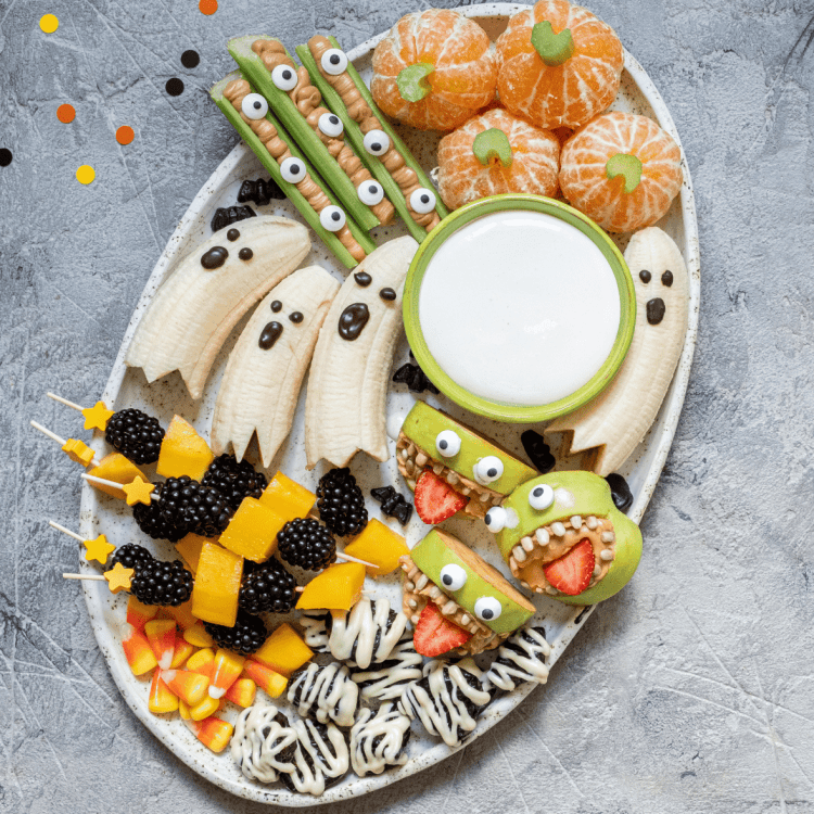 A large plate of healthy halloween recipes like banana ghosts, pumpkin clementines, celery fingers and apple monsters