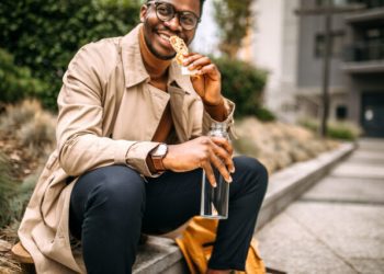Man eating a granola bar while sitting in front of building