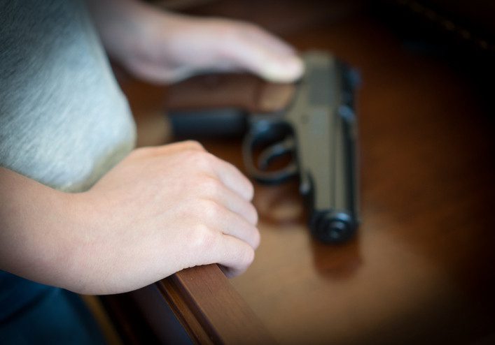 Close up of child's hand on gun in open drawer