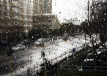 Raindrops rolling down a windowpane on a gray rainy day in a city