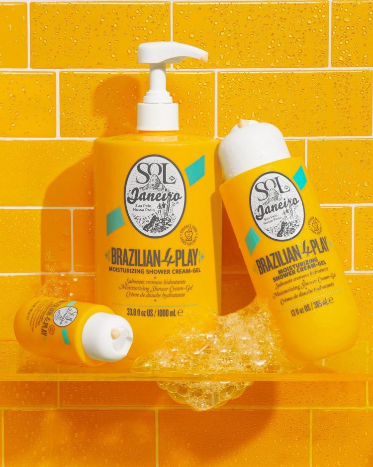Three differentsized bottles of Sol de Janeiro Brazilian 4Play Moisturizing Shower CreamGel with sudsy bubbles leaning...